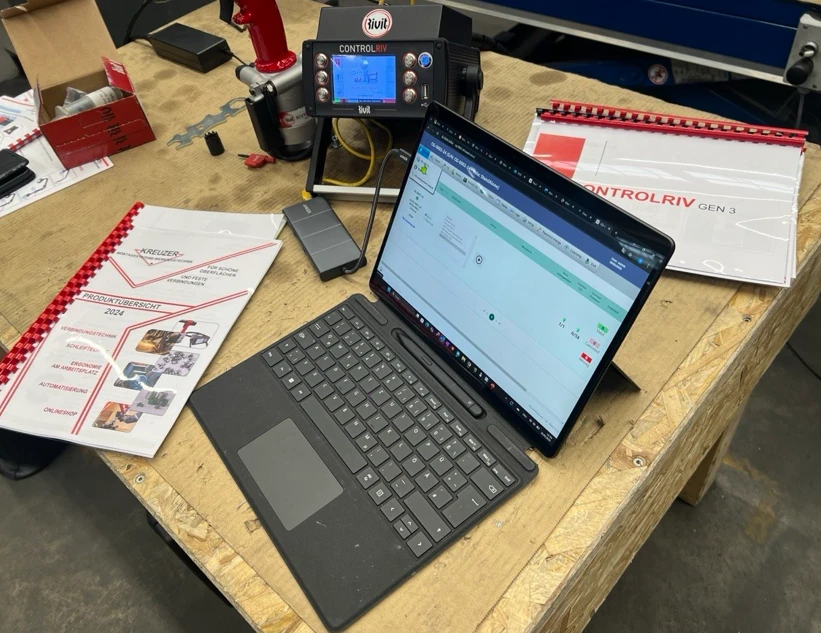 ControlRiv-Prozessüberwachung in der Werkstatt: Laptop mit Software-Oberfläche, ControlRiv-GEN-3-Bedieneinheit und Rivit-Produktkatalog auf einer Werkbank.